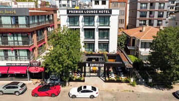 Un hotel con un letrero destacado para el Premier Lounge Hotel, una cafetería llamada Cuppresso y varios coches estacionados frente a él.