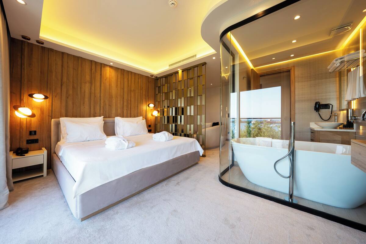 A modern bedroom with a large bed, a glass-enclosed bathtub, and a view of the outdoors.
