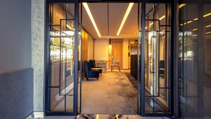 Un moderno vestíbulo de hotel con puerta de cristal, piso alfombrado y un área de descanso con sillas.