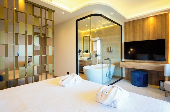 A modern hotel room with a large bed, a bathtub, a TV, and a glass partition. - Premier Lounge Hotel (Tuzla)