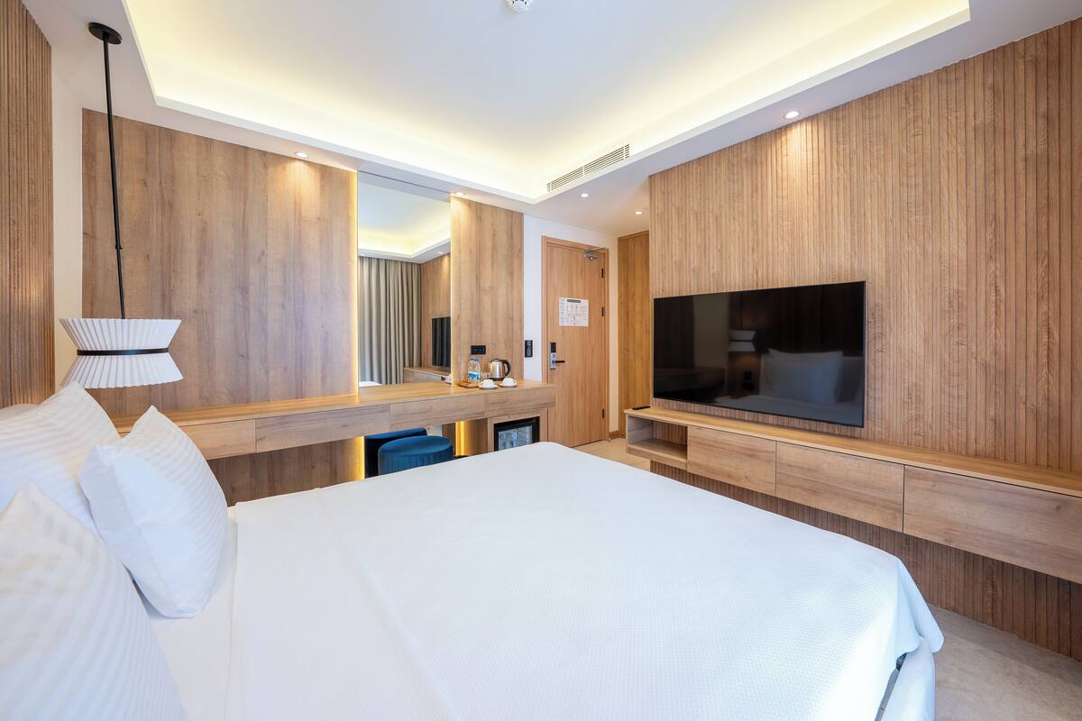A modern hotel room with a large bed, a TV, a mirror, and wooden paneling.