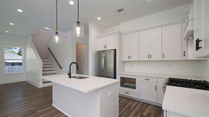 A modern kitchen with white cabinetry, a central island, stainless steel appliances, and a staircase leading to another level.