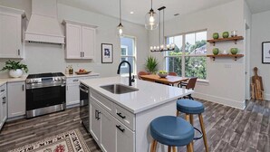 A modern kitchen with white cabinetry, a stainless steel stove, and a large island with bar stools.