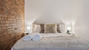 Un dormitori amb pared de maó, un llit amb roba de llit blanca i un almoïna mullada, i dues làmpades de nit.