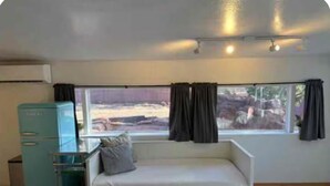 Een kamer met een bed, een raam met gordijnen, een kitchenette en uitzicht op een rotsachtig landschap.