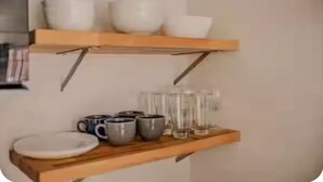 Een keuken met houten planken waarop kommen, bekers en glazen staan.