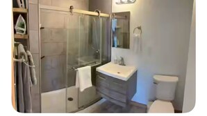 Een moderne badkamer met een douchecabine van glas, een wastafel met spiegel en een toilet.