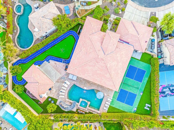 An aerial view of a resort with multiple swimming pools, tennis courts, and a large covered area.