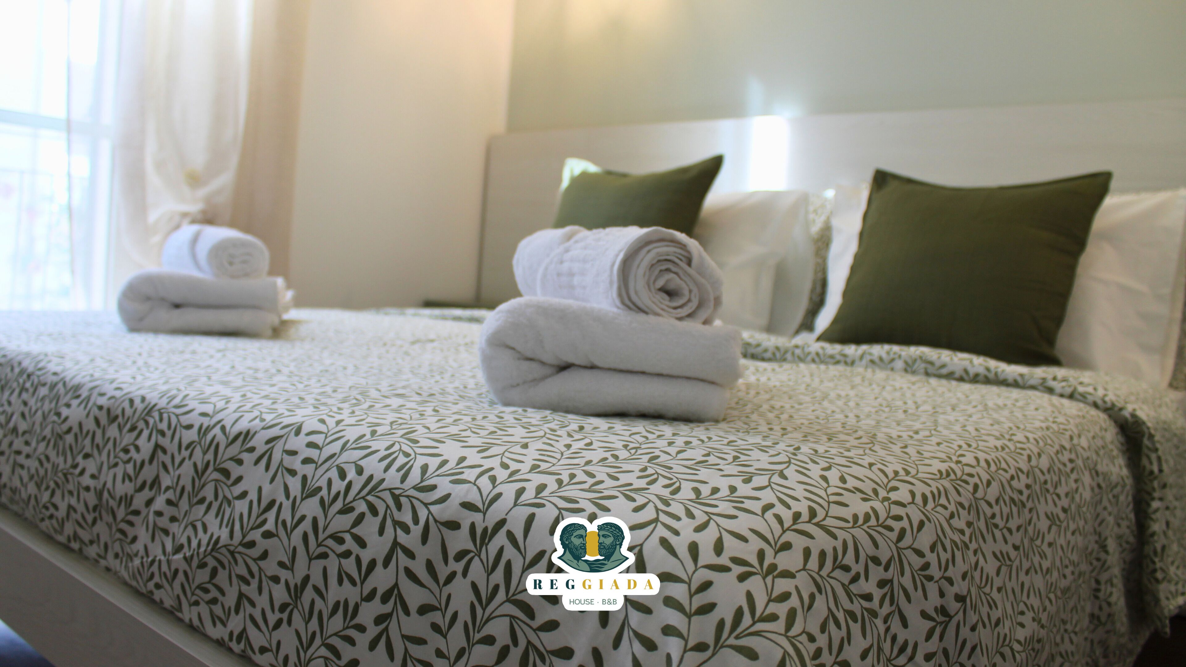 Una cama bien tendida con toallas enrolladas, una colcha estampada y almohadas verdes en una habitación de hotel.