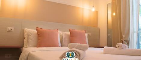 A hotel room with a neatly made bed, two pillows, a towel, and a mirror.
