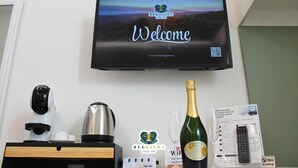 En hotellreception med en tv-skärm som visar ett välkomstmeddelande, en flaska champagne, en fjärrkontroll och en skylt som visar att det finns Wi-Fi.