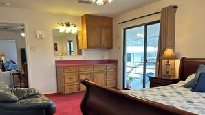 A bedroom with a bed, a chair, a wooden cabinet, a mirror, and a sliding glass door leading to a balcony. - Legacy Ranch-Family Reunion Facility. Four Guest Houses, Recreation Center, & Swimming Pool (Mason)
