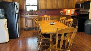A compact kitchen with wooden cabinets, a black refrigerator, a microwave, a stove, and a dining table with chairs. - Legacy Ranch-Family Reunion Facility. Four Guest Houses, Recreation Center, & Swimming Pool (Mason)