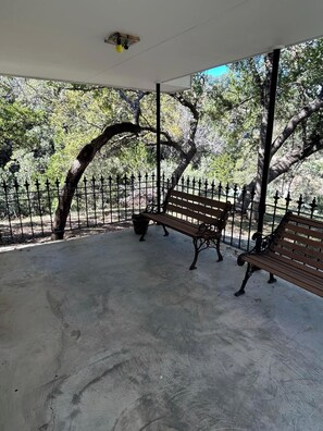 A covered outdoor area with a concrete floor, two wooden benches, and a metal fence. - Legacy Ranch-Family Reunion Facility. Four Guest Houses, Recreation Center, & Swimming Pool (Mason)