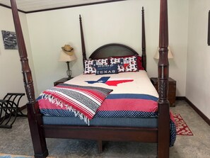 Una cama con dosel, con un edredón con motivos de Texas, una lámpara y una mesita de noche.