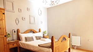 A bedroom with a wooden bed, a nightstand, a radiator, and a wall with framed pictures. - This is a double room with a double bed. It has an en-suite bathroom. The window in the room looks out into the hallway. (Vilaflor)