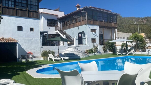 A poolside area with a pool, white lounge chairs, and a staircase leading to a building with a tiled roof. - This is a double room with a double bed. It has an en-suite bathroom. The window in the room looks out into the hallway. (Vilaflor)