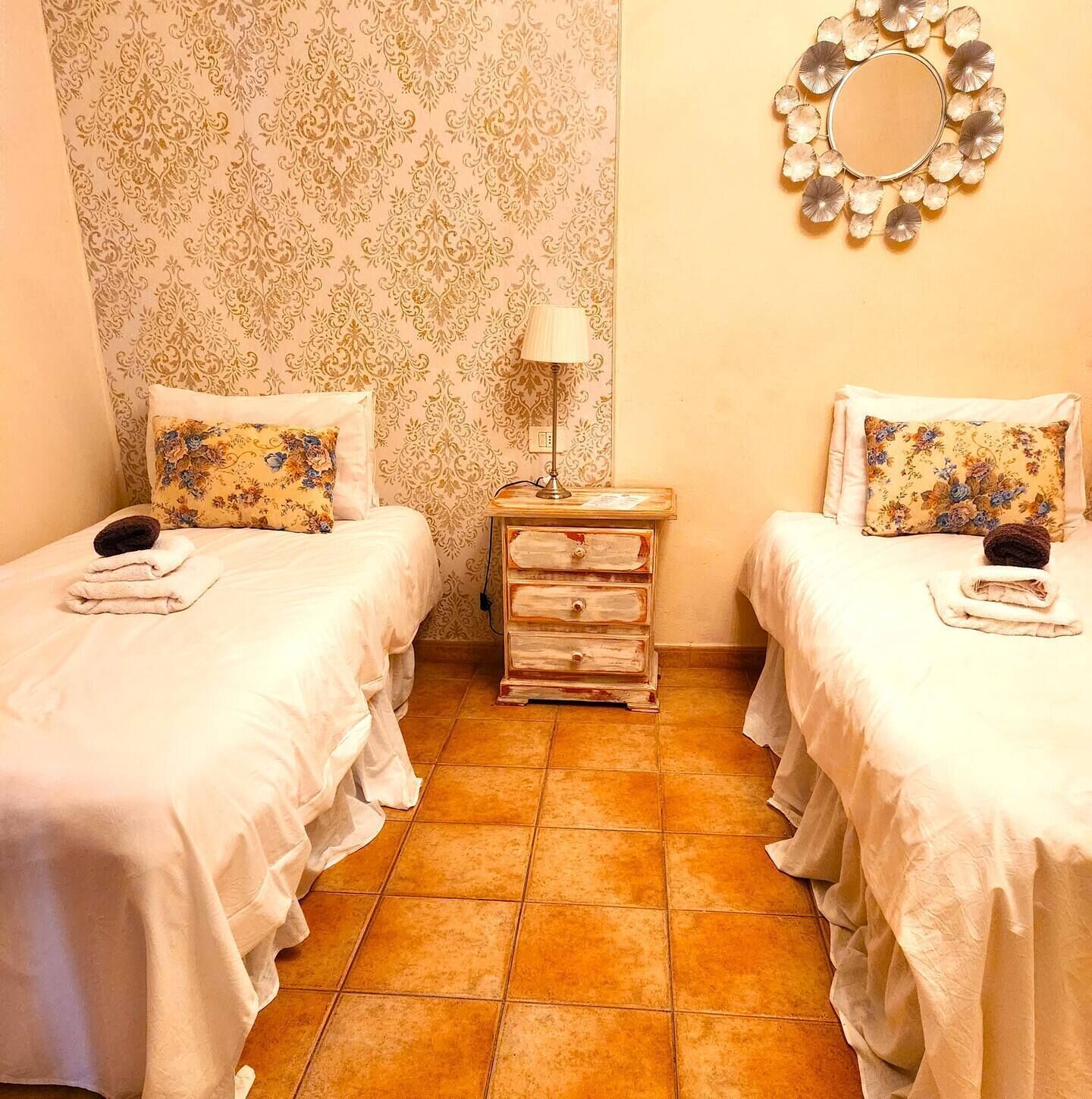 Una habitación con dos camas, cada una con un cojín floral y una mesita de noche con lámpara.