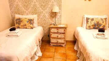 Una habitación con dos camas, cada una con un cojín floral y una mesita de noche con lámpara.