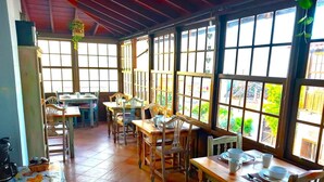 Un comedor amplio con mesas y sillas de madera, ventanas grandes y piso de baldosas.