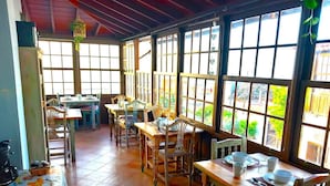 Un comedor amplio con mesas y sillas de madera, ventanas grandes y piso de baldosas.