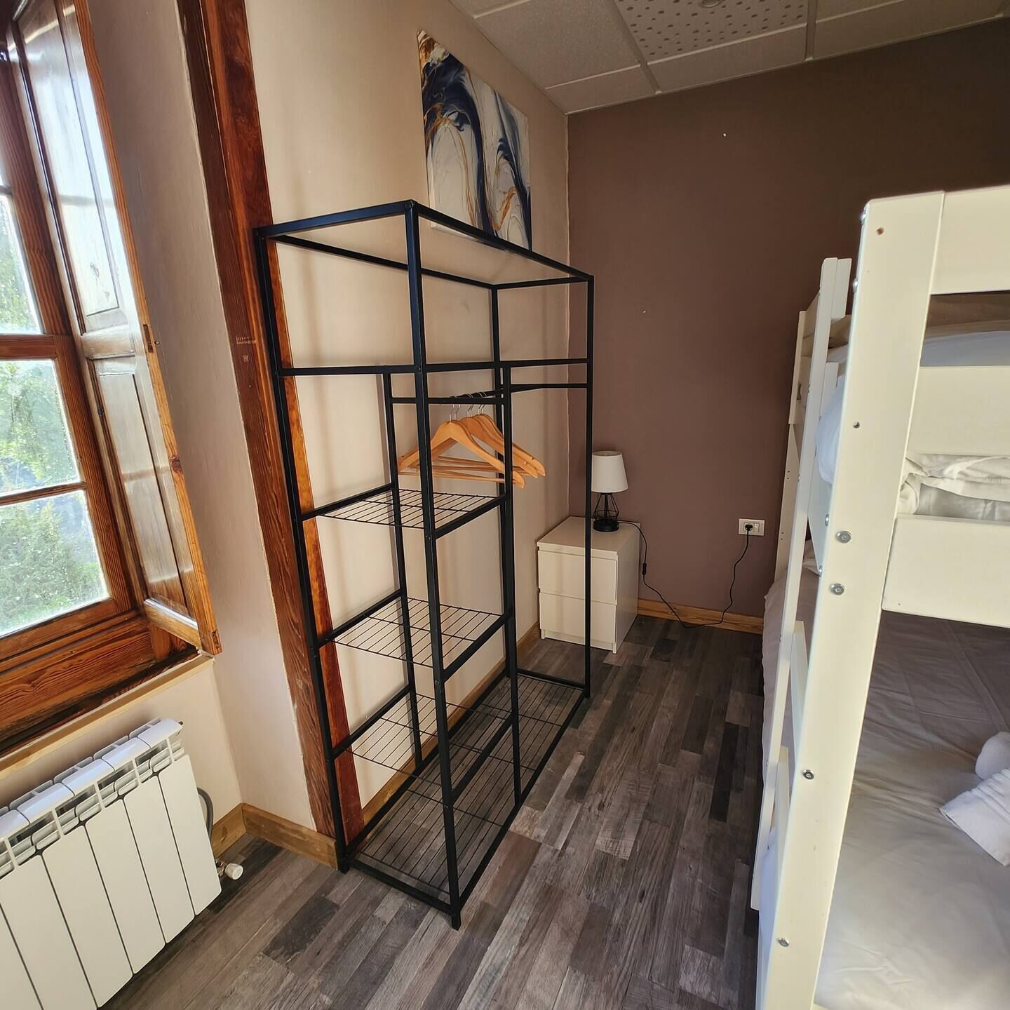 Een kamer met een stapelbed, een metalen rek, een radiator en een raam.
