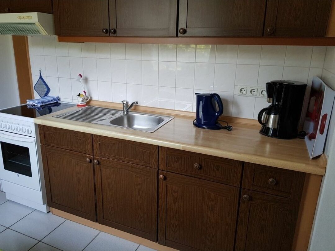 Una cocina con armarios de madera, un lavamanos de acero inoxidable, una cafetera y una estufa.