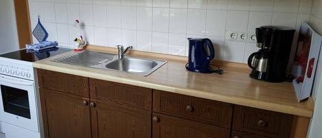 Una cocina con armarios de madera, un lavamanos de acero inoxidable, una cafetera y una estufa.