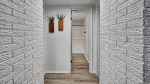 A narrow hallway with white brick walls and wooden flooring leading to a door. - Family-Friendly Stay Near OSU & Boomer Lake (Stillwater)