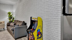 A living room with a white brick wall, a sofa, a coffee table, and a Pac-Man arcade machine. - Family-Friendly Stay Near OSU & Boomer Lake (Stillwater)