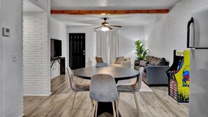 A modern living room with a round dining table, grey chairs, a sofa, and a gaming machine. - Family-Friendly Stay Near OSU & Boomer Lake (Stillwater)