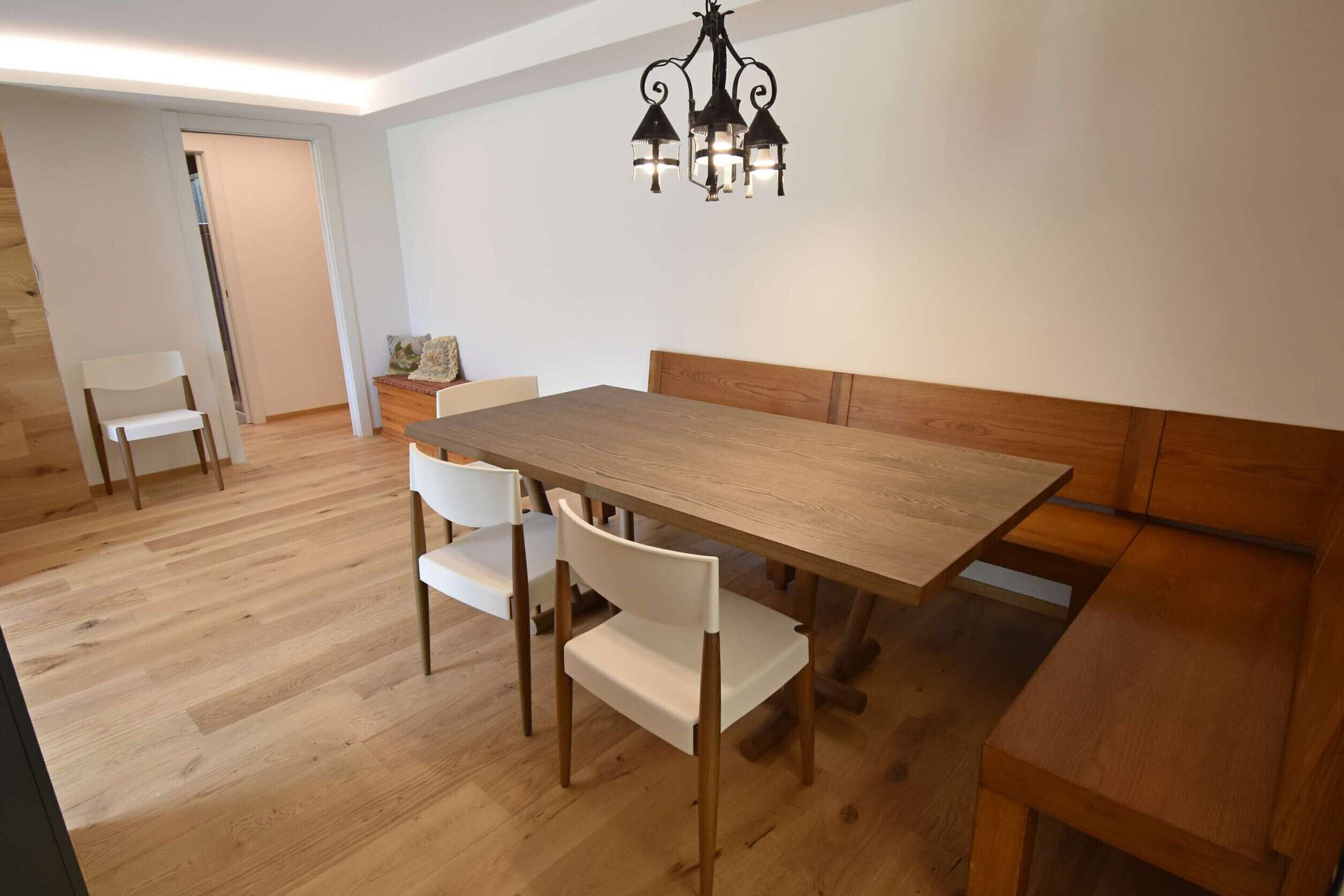 A dining area with a wooden table and chairs, a bench, and a chandelier.