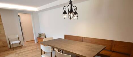 A dining area with a wooden table and chairs, a bench, and a chandelier.