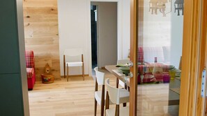 Une cuisine moderne avec un plancher en bois, un coin repas avec des chaises blanches et un canapé à carreaux rouges.