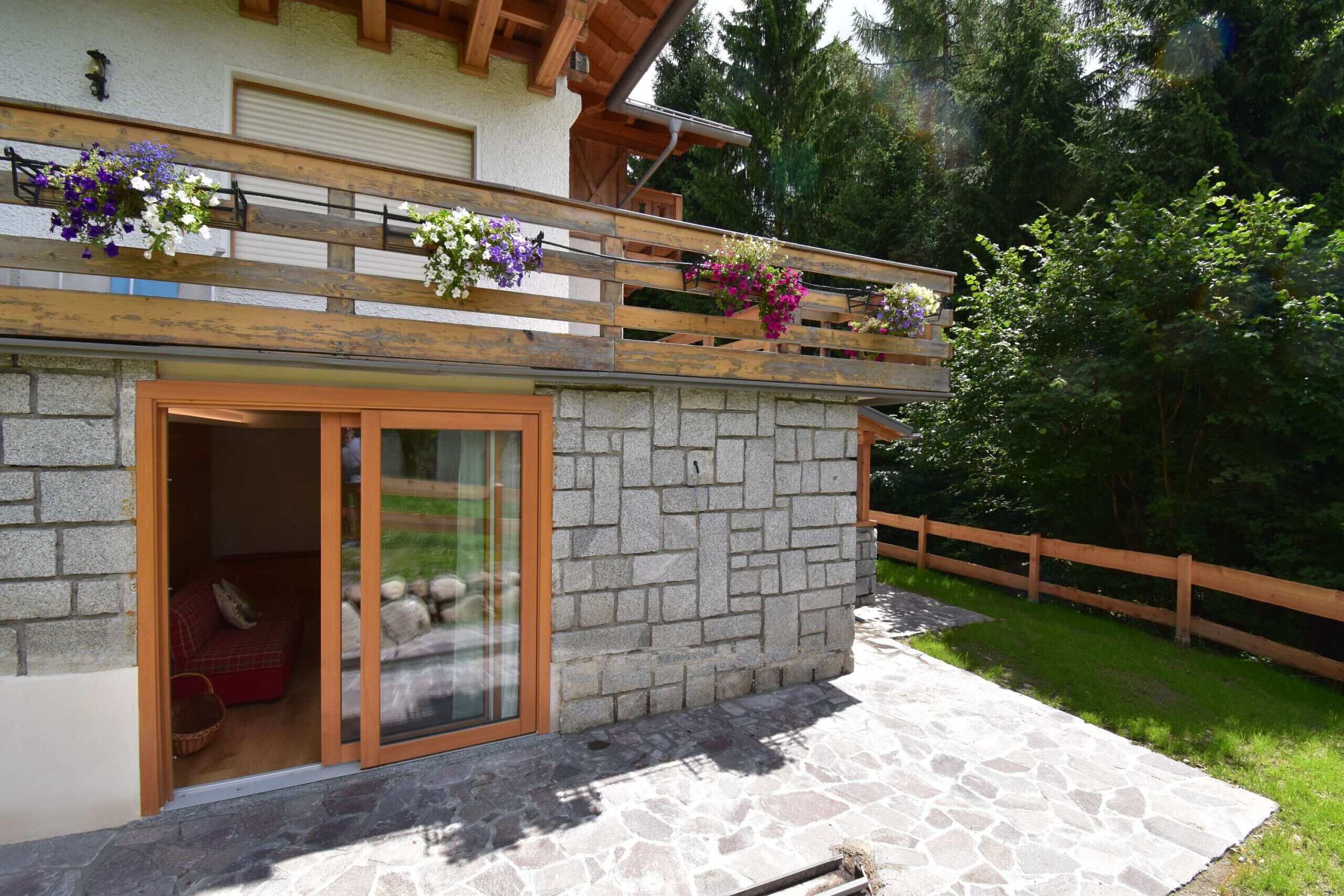 A stone building with a wooden balcony, a sliding glass door, and a stone patio.
