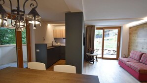 Un coin repas avec une table et des chaises en bois, une cuisine à l’arrière-plan et un canapé rouge dans l’espace salon.