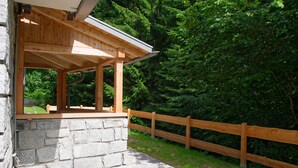 Une structure en bois avec des murs en pierre, un chemin en pierre et une clôture en bois, située dans une zone boisée.