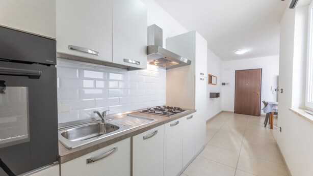 Une cuisine moderne avec des armoires blanches, un évier en acier inoxydable et une cuisinière à gaz.