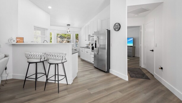 A modern kitchen with white cabinetry, a stainless steel refrigerator, and a bar area with two stools. - Chic happens 3/2 heated pool 5 min from Siesta (Sarasota)
