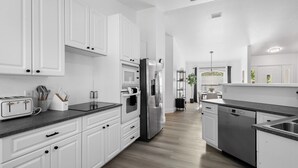 A modern kitchen with white cabinets, stainless steel appliances, and a black countertop. - Chic happens 3/2 heated pool 5 min from Siesta (Sarasota)