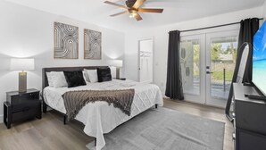 A modern bedroom with a large bed, two bedside tables, a ceiling fan, and a view of the outdoors through a sliding glass door. - Chic happens 3/2 heated pool 5 min from Siesta (Sarasota)