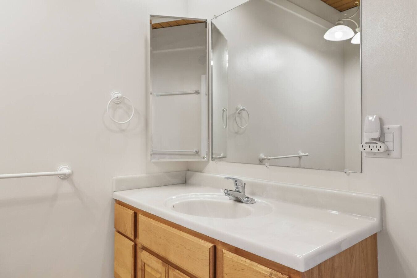 A bathroom with a white sink, wooden cabinets, a mirror, and a towel rack.