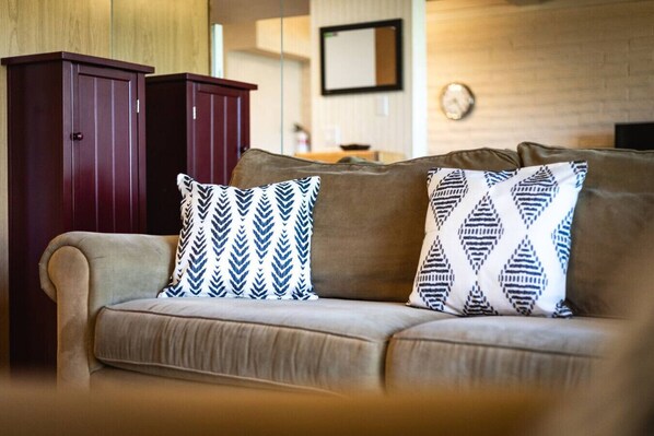Un sofá color beige con dos almohadones estampados y un mueble de madera oscura en una sala de estar.