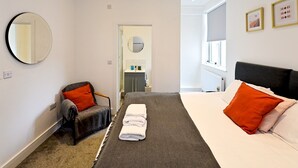 A modern hotel room with a bed, a chair, a mirror, and a bathroom visible through an open door. - Pass the Keys | Llandaff - Modern, Bright & Central w/Parking (Cardiff)