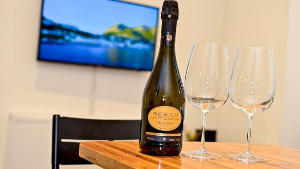 A bottle of Prosecco wine and two empty wine glasses on a wooden table with a television in the background. - Pass the Keys | Llandaff - Modern, Bright & Central w/Parking (Cardiff)