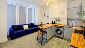 A compact kitchen with a washing machine, a wooden countertop, and a blue sofa with cushions. - Pass the Keys | Llandaff - Modern, Bright & Central w/Parking (Cardiff)