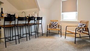 A modern kitchen with a dining area, featuring a high ceiling, recessed lighting, and a large window with a blind. - Roath - Modern Flat Near City Centre W/Parking | Pass the Keys (Cardiff)