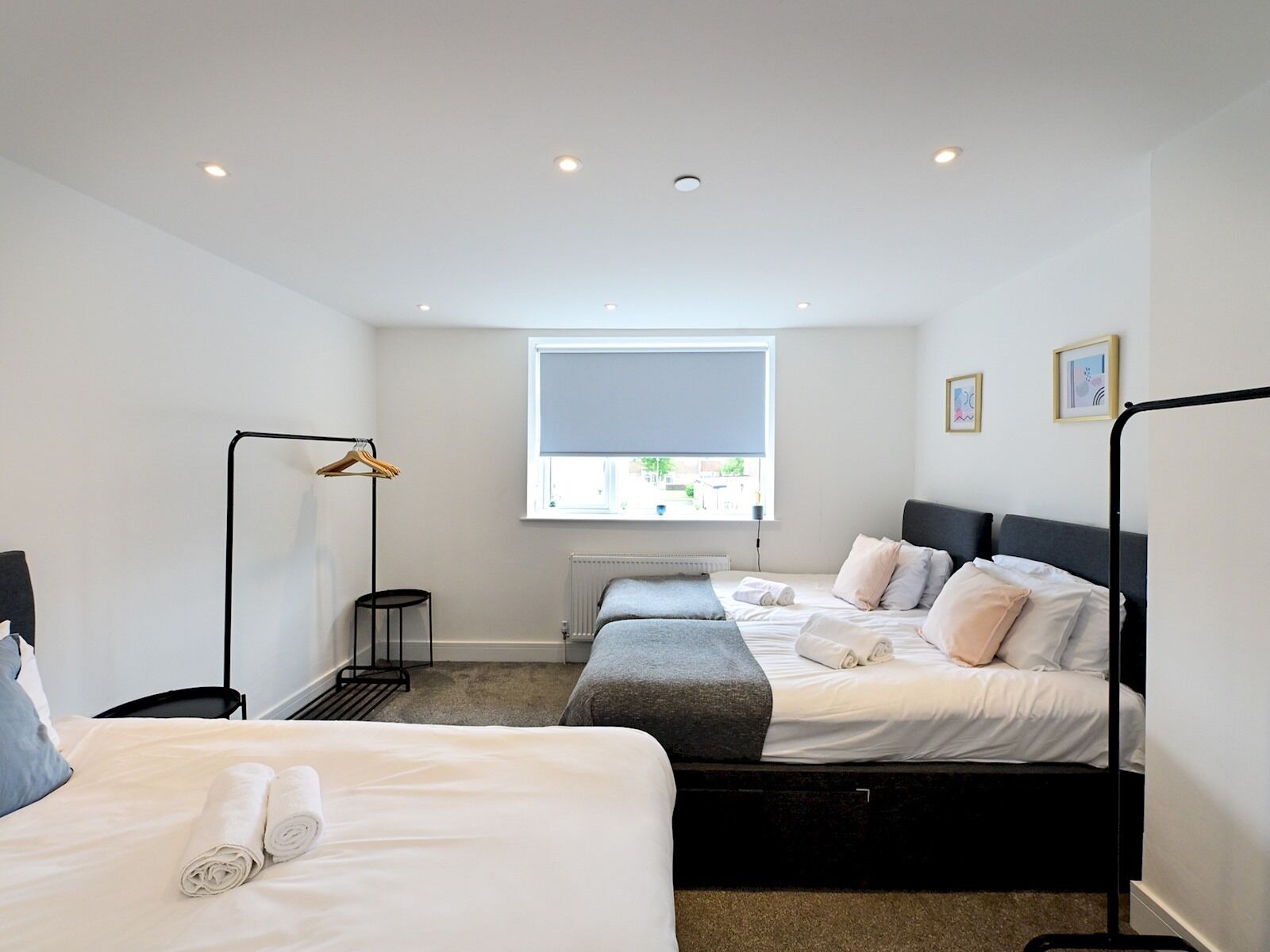 A modern hotel room with two beds, a standing lamp, a radiator, and a window with a view.