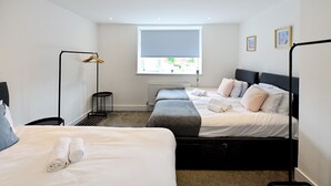 A modern hotel room with two beds, a standing lamp, a radiator, and a window with a view.