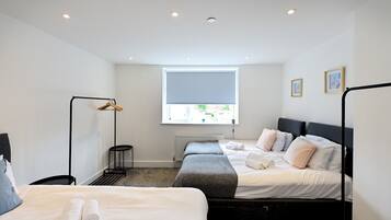 A modern hotel room with two beds, a standing lamp, a radiator, and a window with a view.